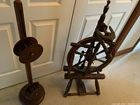 Antique wooden spinning wheel standing next to a squirrel cage swift against a white door background.