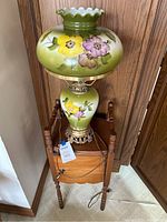 Full view of table with lamp on top showing floral painted ceramic lamp and wood table with cupboard below.