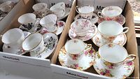Box with twelve teacups and matching saucers in floral patterns with gold trim, arranged in two rows.
