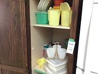 Shelf with yellow, green, white, red, and orange Tupperware containers, the smaller white cup holder, and a yellow juicer accessory