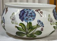 Side view of the white porcelain bowl featuring botanical illustrations of blue flowers and butterflies, showing no chips or cracks.