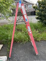 Full view of the Louisville fiberglass folding ladder showing its A-frame style and red fiberglass sides outdoors with greenery background.