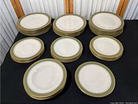 Photo of the full collection including stacks of 17 10-inch plates, 9 8-inch plates, and 4 bowls, showing green and gold decorative borders