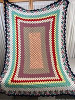 Full view of the hand crocheted blanket showing its multicolor granny square pattern and scalloped edge.