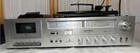 Front view of Hitachi stereo unit showing cassette player, radio tuner dial, and control knobs.