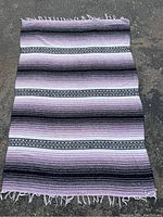 Full view of handwoven rug or blanket laid flat showing horizontal stripes and fringes.