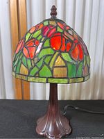 Full view of the lamp showing the stained glass shade with red tulips and green leaves, and the dark metal base.