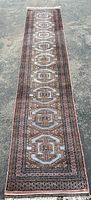 Full length of long narrow vintage wool runner rug laid on outdoor surface showing entire design and color tone.