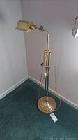 Full view of the brass-finished adjustable metal floor lamp standing on carpeted floor.
