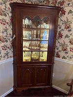 Closed front view of wooden corner hutch cabinet showing glass door and wood panel lower doors.