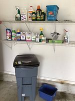 Photo showing garden chemical bottles and supplies on two wire shelves above the trash can in garage setting