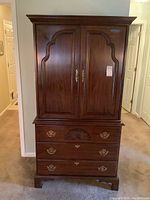 Front view of entire cherry wood armoire showing doors closed and three drawers below