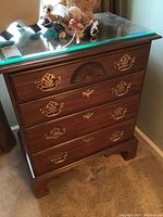 Full front view of nightstand showing cherry wood finish, four drawers, brass hardware, and beveled glass top protector