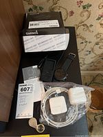 Garmin Approach S60 watch, original refurbished box, two chargers, and loupe on table showing lot contents.