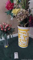 Yellow and white ceramic umbrella stand filled with colorful faux flowers including pink, yellow, and brown hues.