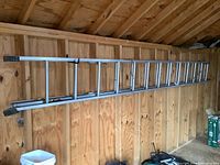 Full view of metal extension ladder extended in a wooden shed, showing length and condition.