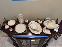 Top view of eleven Lenox porcelain pieces arranged on a dark wooden table, highlighting swan figurines, bud vases, dishes, and decorative plates.