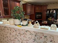 View of 9 ceramic items including planters, votives, and decorative baskets arranged in a row on kitchen counter.