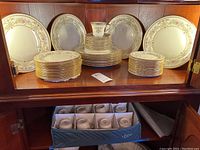 Full view of stacked dinner plates, salad plates, bread plates, cups and saucers in wooden cabinet