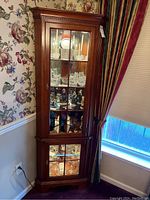 Photo of the closed wood corner display cabinet with light on showing glass shelves and mirrored back