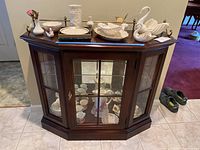 Overall view of the dark wooden lighted curio cabinet with glass front door and side panels, showing contents inside the cabinet, which are not included in sale.