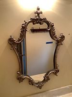 Full view of the wall mirror hanging on a wall, showing ornate carved frame and reflective glass surface.
