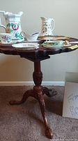 Photo of the table top and leg structure showing carved claw feet and pie crust edge with various ceramic items on top, but contents excluded from lot sale.