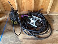 Photo showing coiled heavy duty black hose with attached spray gun fittings including purple and green connectors on wood floor.