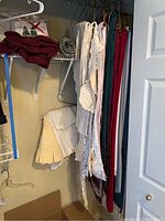 Photo showing hanging table linens including runners and lace pieces in various fabrics and colors like burgundy, cream, and white.