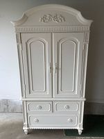 Front view of white Thomasville armoire media center showing ornate carved top, double paneled doors, and three drawers below
