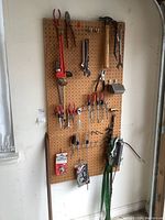 Wide view of assorted hand tools hung on pegboard including pipe wrench, screwdrivers, pliers, hammer, tubing cutters, and sprays