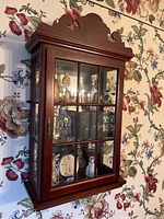 Front angle photo of wooden wall cabinet showing glass front and side panels, mirrored back seen through.