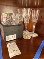 Full view of four tall Waterford crystal champagne glasses and one Waterford crystal coaster on black box. All items acid etched, glasses approximately 8.75 inches tall.