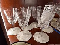 Set of six Waterford crystal stemware glasses arranged on white doilies, showing overall condition and design