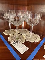 Four clear crystal goblets arranged on crocheted doilies inside a wood cabinet.