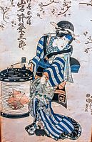 Close-up photo of the antique Japanese woodblock print showing a woman in traditional kimono holding a lantern, displaying detailed patterns and calligraphy.