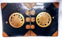 Front view of the document holder showing lacquered wood surface with large circular brass medallions depicting human profiles and brass corner decorations.