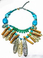 Photo showing entire vintage multi strand necklace with mixed turquoise stones, green beads, and gold and silver elongated textured pendants.