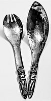 Full view of the pair of salad servers showing fork and spoon with silverplate finish and carved figures on handles.