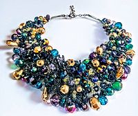 Top angled view of a vintage multi-colored rhinestone bib necklace with gold-tone bead accents laid flat, showing detailed rhinestone clusters and black mesh backing.