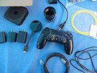 Displayed various electronic accessories organized on blue background: game controller, camera lens, cables, power adapters, optical device.