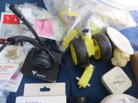 Top view of box showing assorted electronic parts including yellow motors with wheels, a black Yamay headset device, and other components in plastic bags and packaging.