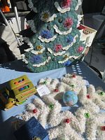 Metal Christmas tree decoration showing front with flower-shaped decorations and white trim, placed on a blue table.