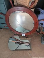 Large ship wheel mirror with wooden spokes visible, laying on floor alongside two smaller mirrors