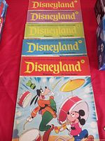 Eight Disneyland magazines stacked showing colorful character covers including Mickey Mouse, Goofy and Donald Duck, all for young readers in various bright cover colors.