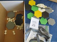 Modular hexagon clock pieces in various colors and clock hands, laid out on a blue surface, some stored in a cardboard box.