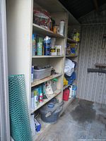 Full view of two white metal shelving units containing garden supplies and chemicals in a garden shed, with visible wear and rust.