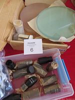 Box containing various microscope eyepieces and old telescope lenses. Several eyepieces are wrapped in plastic. Cardboard box contains large round lenses and smaller optical components.