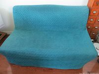 Front view of a blue loveseat size futon with textured fabric cover in used condition.