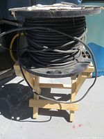 Full view of large black plastic wire spool resting on a wooden stool outdoors with some wire extended.